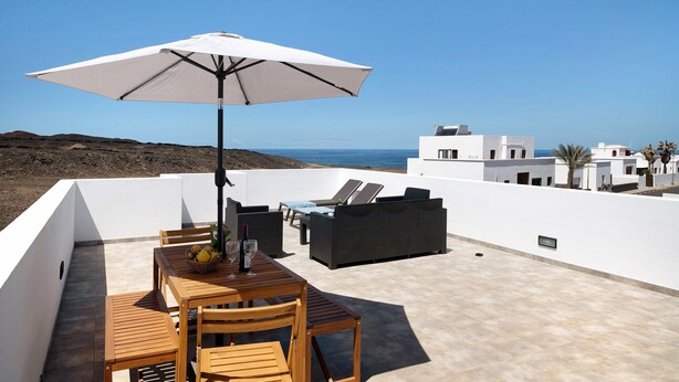 Une terrasse sur le toit, avec une table, des chaises, un canapé et un parasol.