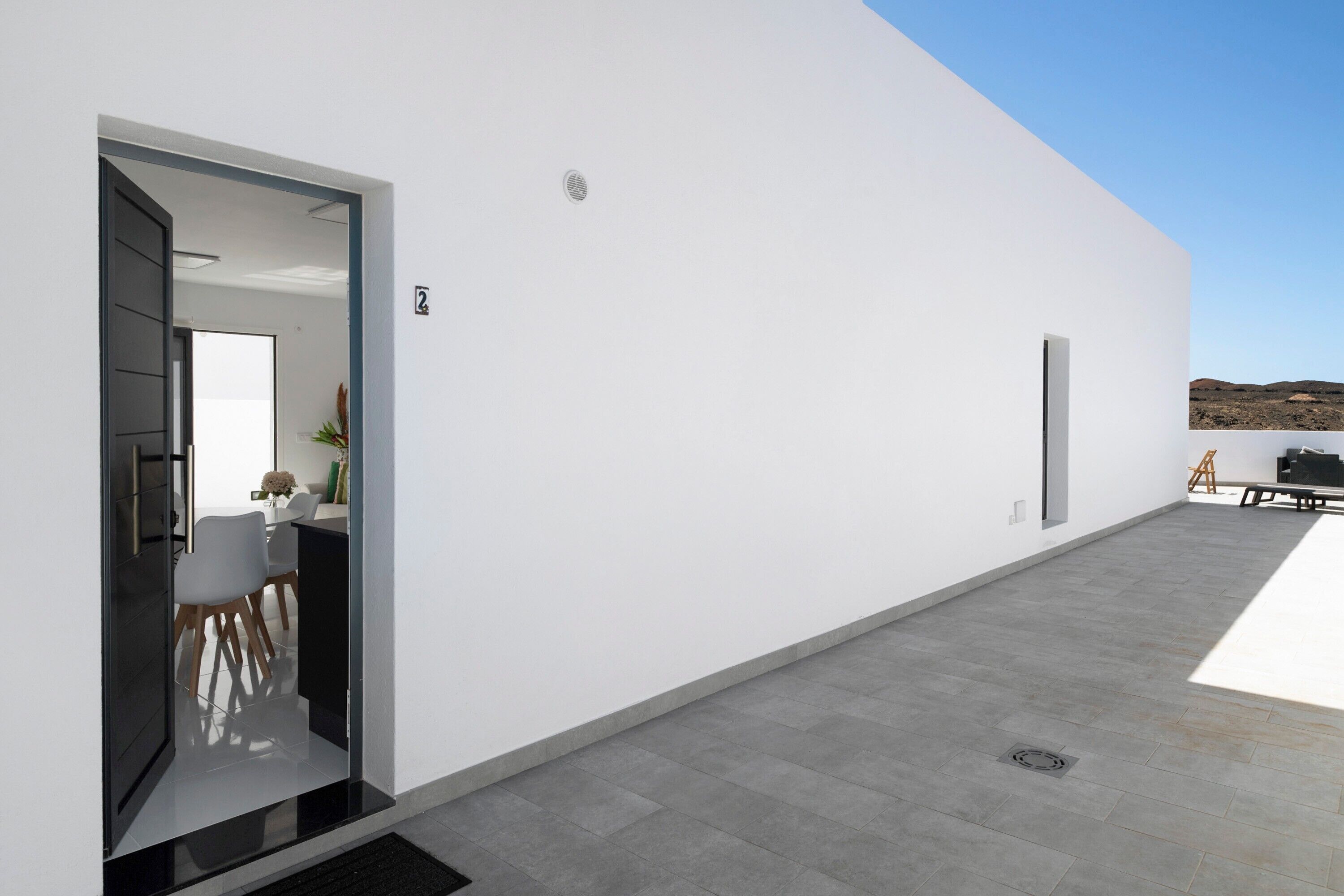 Un bâtiment moderne doté d’un toit plat, d’un espace repas avec des chaises et une table, et un ciel dégagé.
