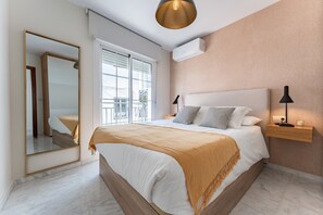 A bedroom with a large bed, a mirror, a window, and a wall-mounted air conditioner.