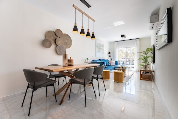 A modern dining area with a wooden table and chairs, a blue sofa, and a large window with a view.