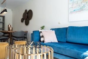 A modern living room with a blue sofa, a glass coffee table with sunglasses, and a wall art piece.