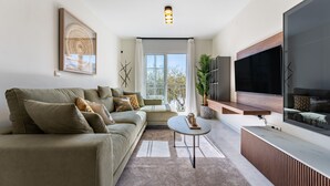Een moderne woonkamer met een bank, salontafel, televisie en groot raam.