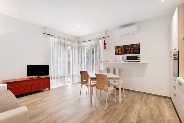 A modern living room with a TV, red cabinet, dining table, chairs, and a kitchen area with appliances.