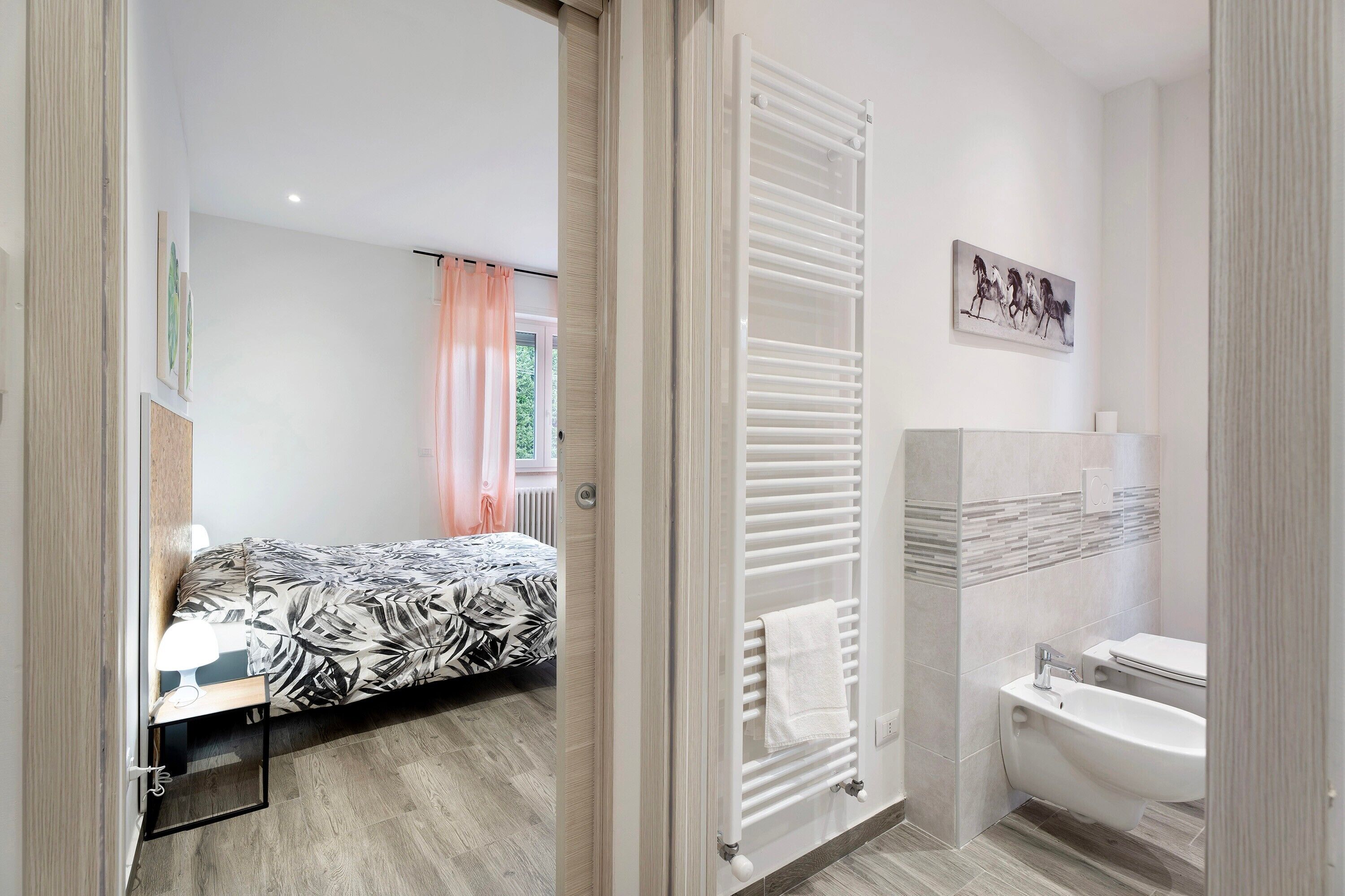 A bedroom with a bed, a bedside table, a radiator, and a bathroom with a toilet and bathtub.