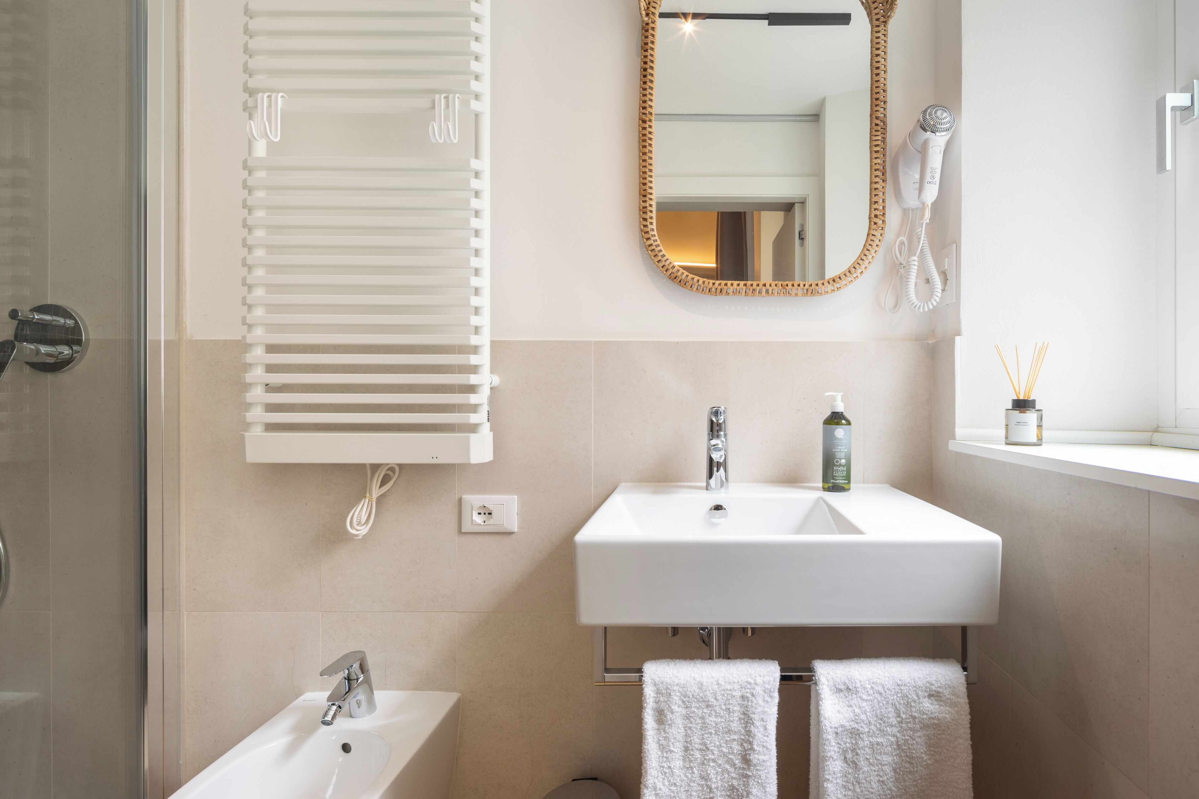 A bathroom with a white sink, a mirror, a hairdryer, and a window with a view.
