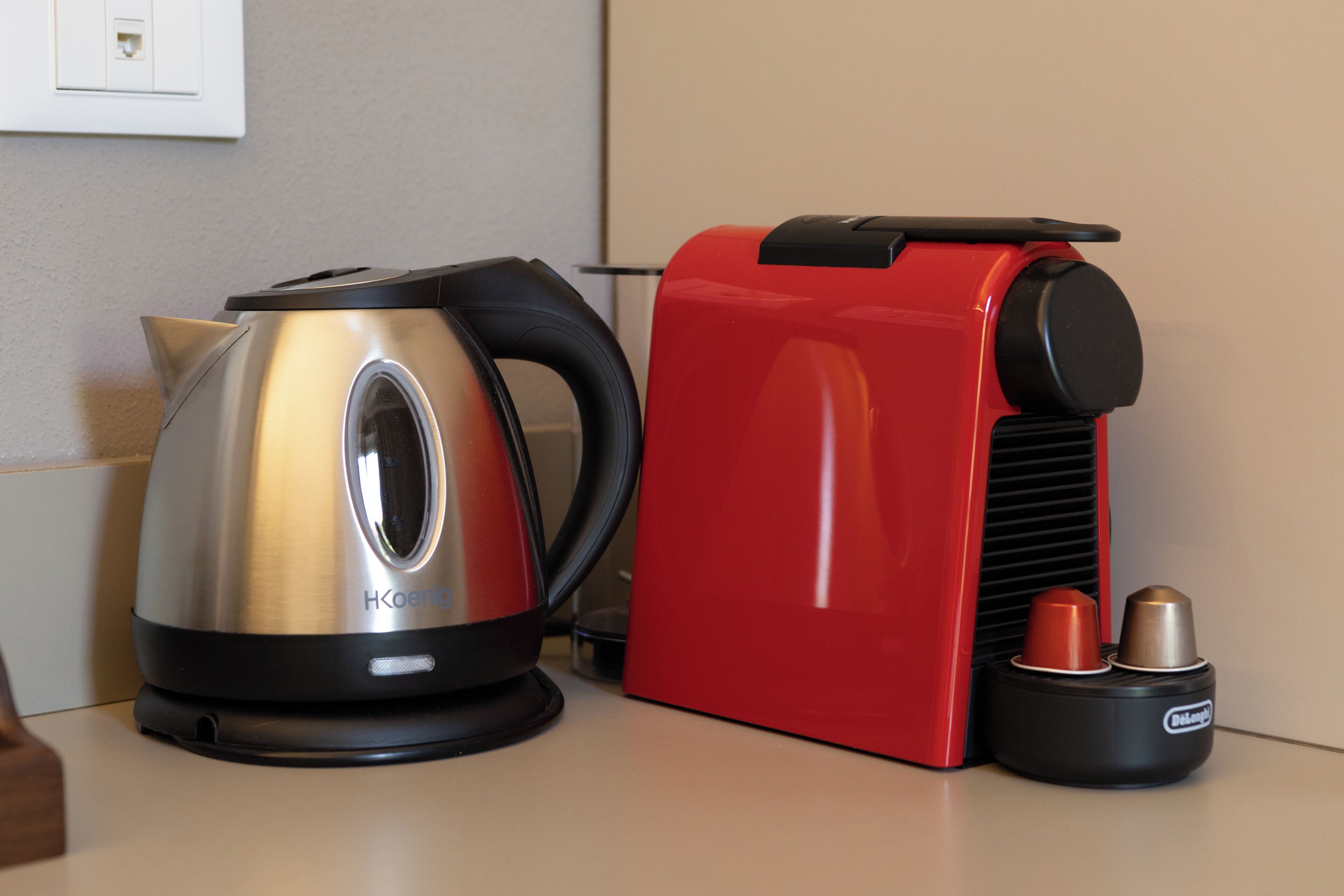 A stainless steel kettle and a red coffee maker on a countertop.