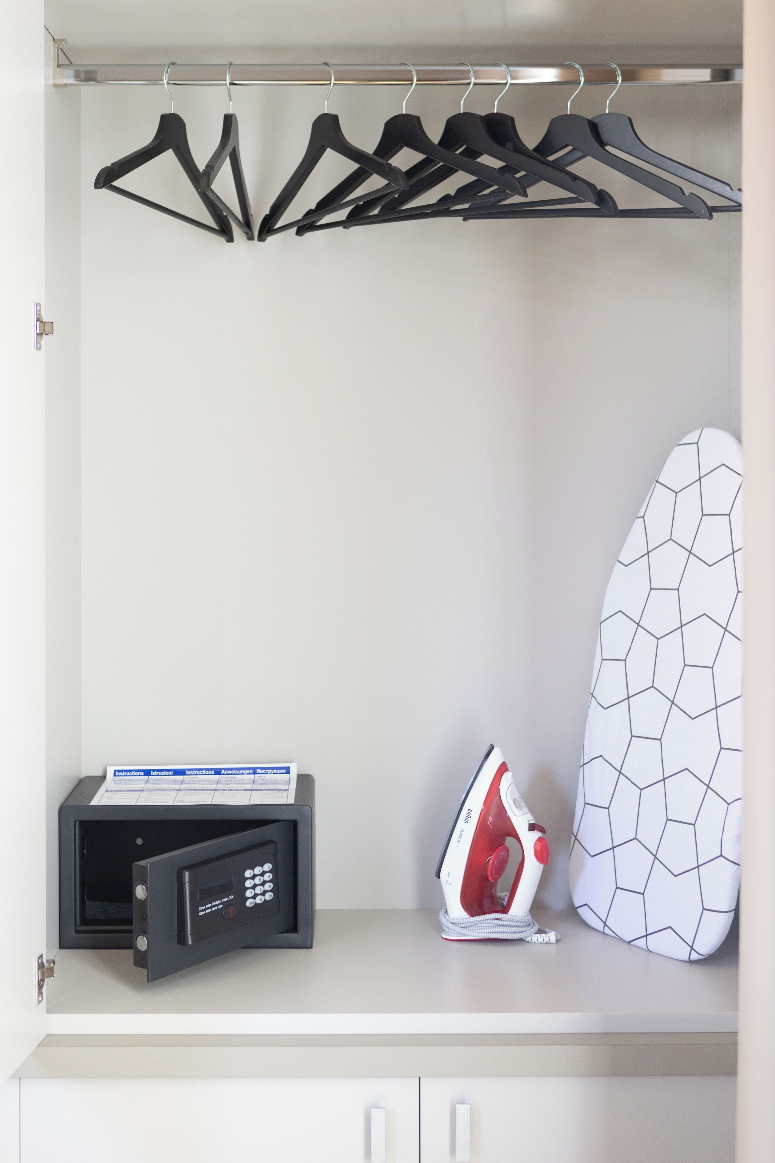 A closet with black hangers, a white ironing board, and a black iron.