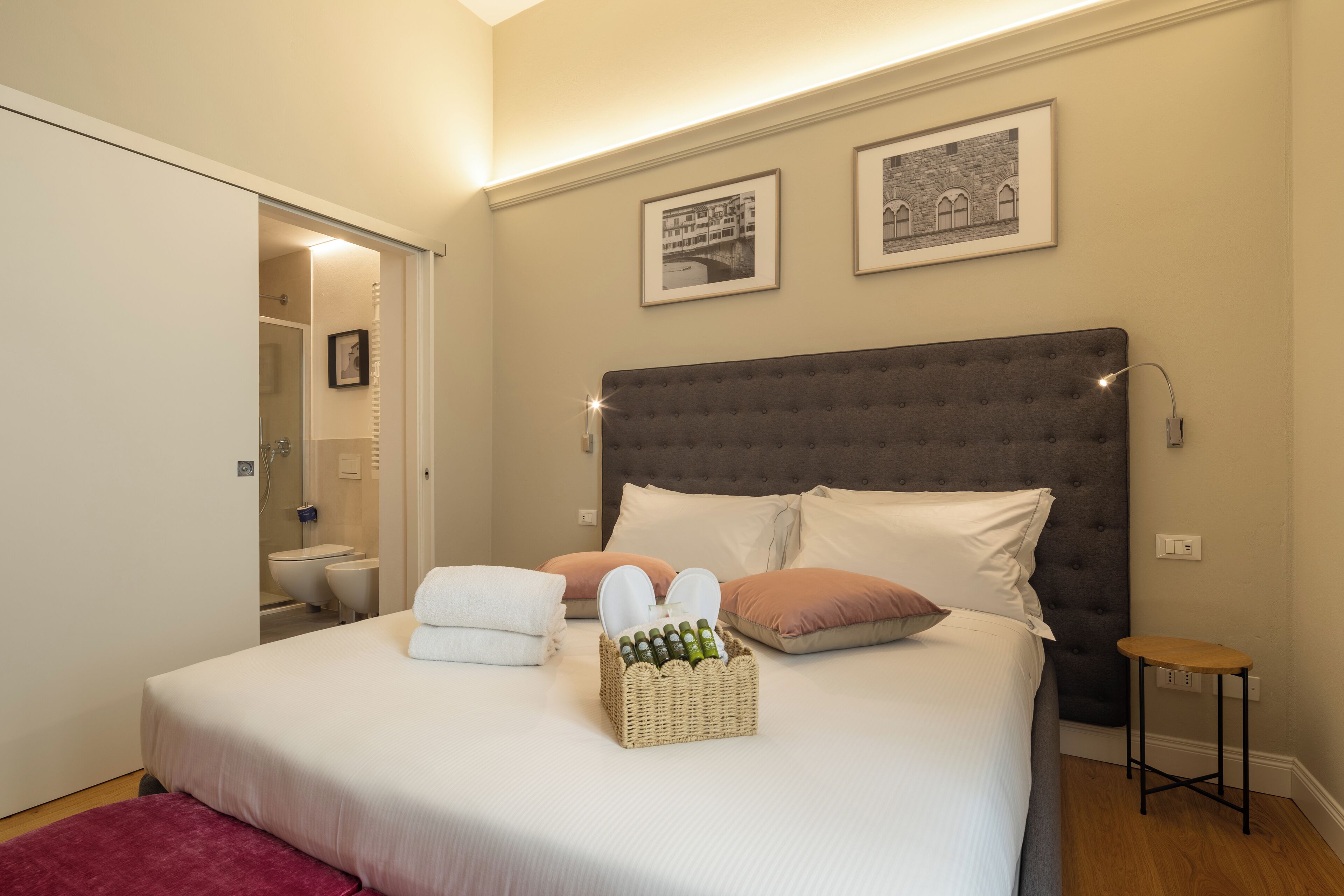 Een net opgemaakt bed met hoofdbord, nachtkastje en een klein krukje.