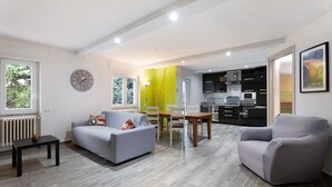 Uma sala de estar moderna com sofá, mesa de jantar e cozinha ao fundo.