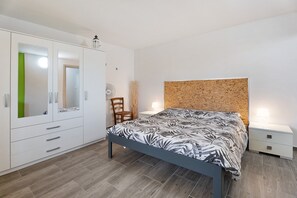 A bedroom with a bed, a wardrobe, a chair, and a nightstand with a lamp.
