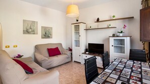 Een woonkamer met een bank, televisie, eettafel en kunstwerken aan de muur.