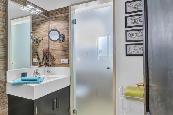 A modern bathroom with a glass shower door, a white sink with a mirror, and a wall-mounted towel rack.
