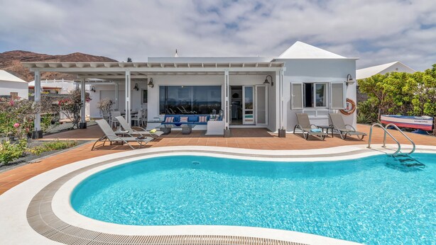 Un hotel moderno con piscina, mobiliario exterior y montañas al fondo.