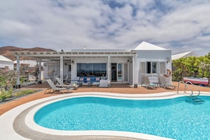 A modern hotel with a swimming pool, outdoor seating, and a mountain backdrop.