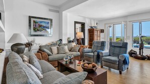 Amplia sala de estar con un sofá grande, sillones, una mesa de centro y vista al mar a través de amplios ventanales.