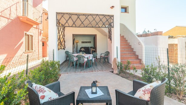 Un patio al aire libre con mobiliario de mimbre, una mesa con un farol y vistas a un edificio con una escalera.