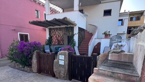 Un patio con una parrilla, piso de baldosas de piedra y un edificio rosa con ventana y puerta.