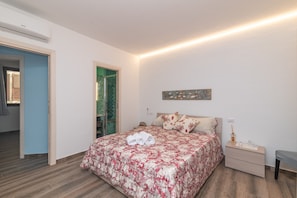 Une chambre à coucher avec une couvre-lit à motifs floraux, une table de chevet avec une lampe et une œuvre d’art accrochée au mur.