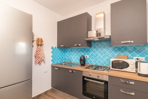 Una cocina moderna con gabinetes grises, un revoque de azulejos azules, una estufa a gas, un microondas y un tostador.