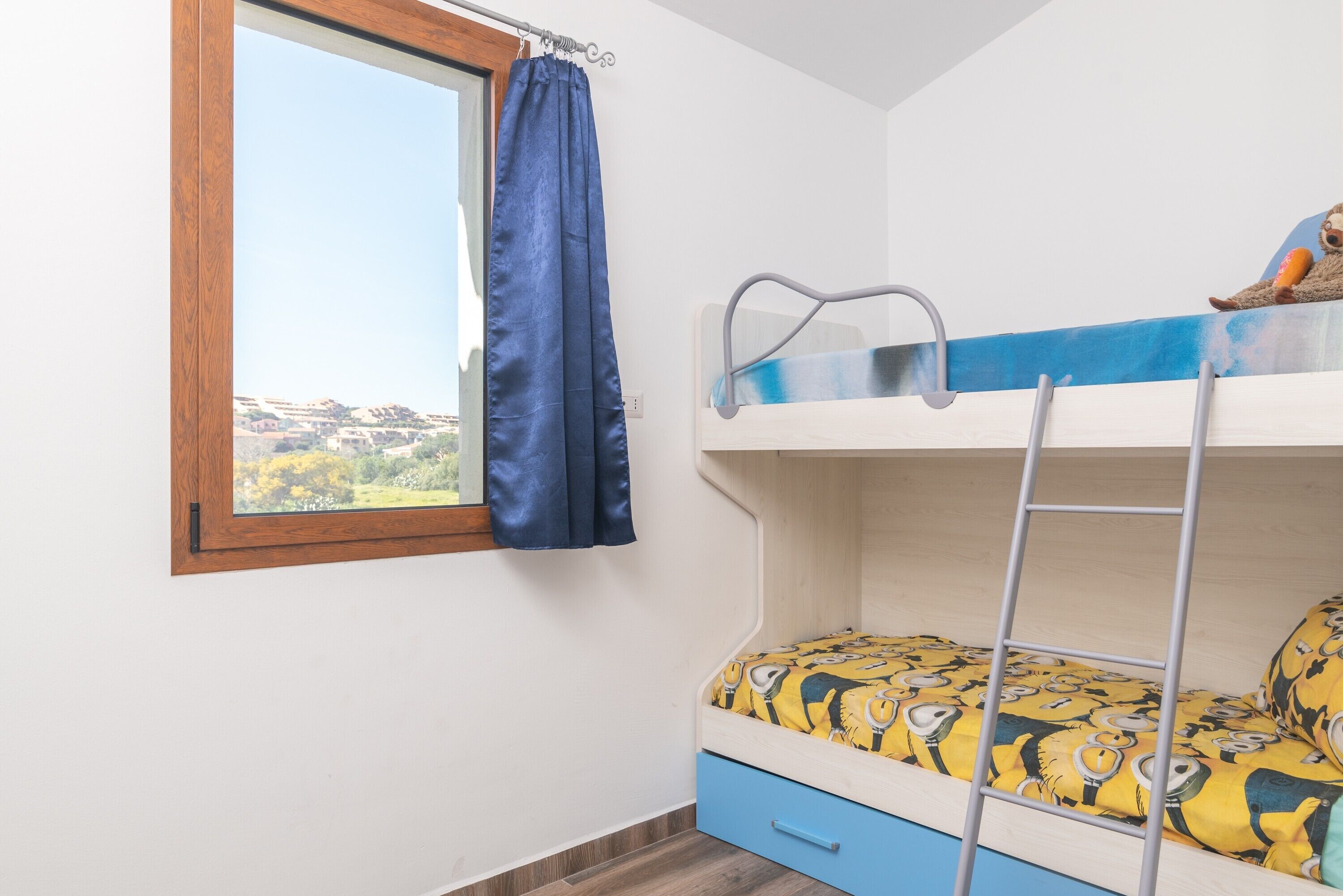 A bunk bed with a ladder, a window with a curtain, and a view of a landscape.