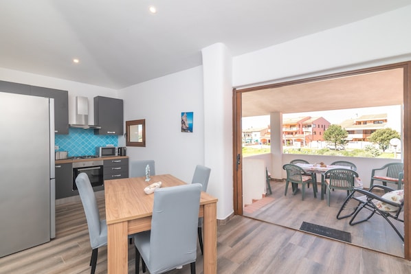A modern kitchen with a dining area, a view of the outside, and a balcony with chairs.