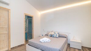 Une chambre à coucher avec un lit, une table de chevet, une porte en bois et une salle de bain visible à travers une porte ouverte.