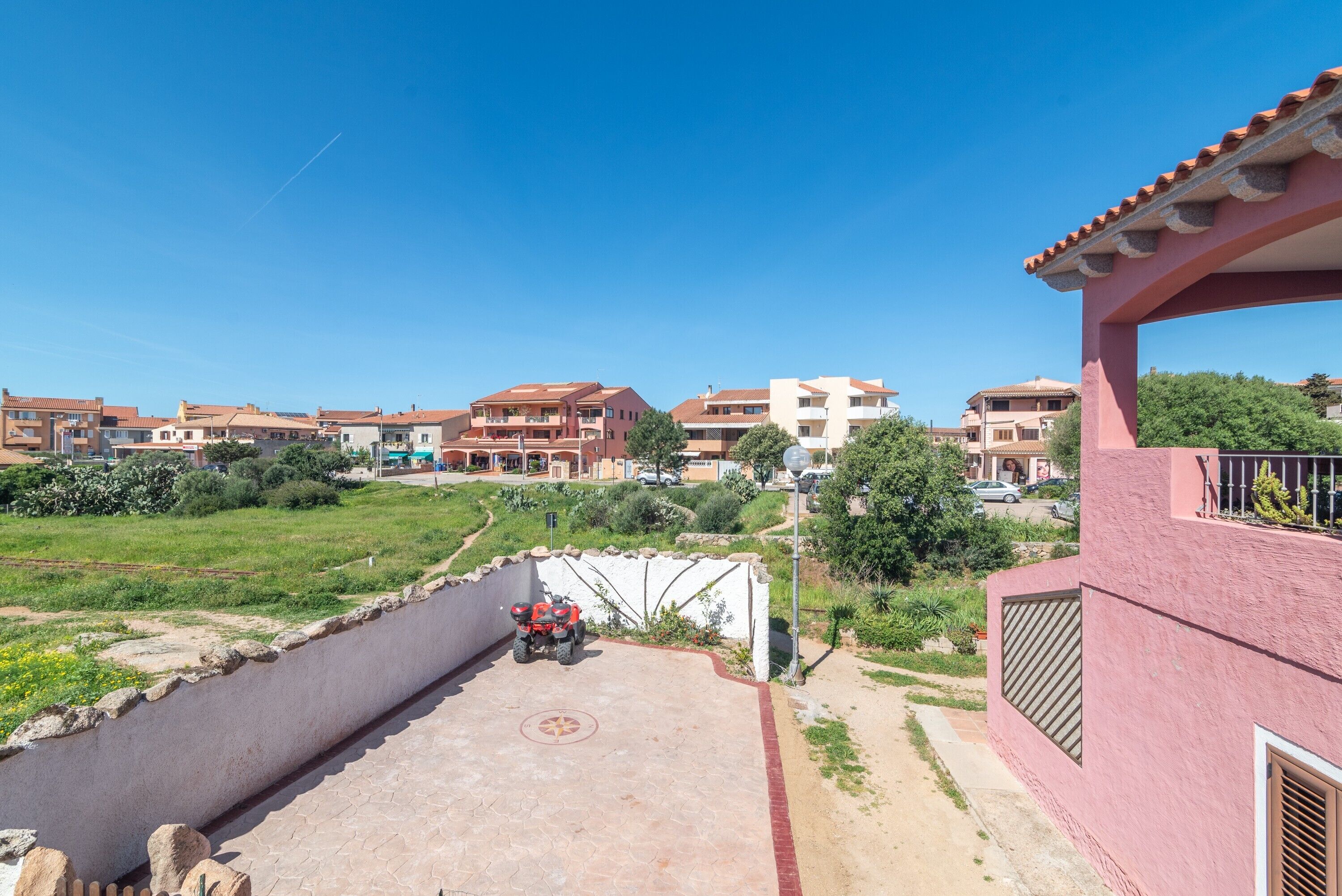 A residential area with a paved driveway, a red vehicle, and buildings with red-tiled roofs.