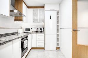 Uma cozinha moderna com armários brancos, forno embutido, micro-ondas, máquina de café e geladeira.