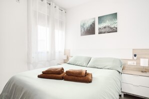 Cama bem arrumada com toalhas, mesa de cabeceira com abajur e duas quadros penduradas na parede.