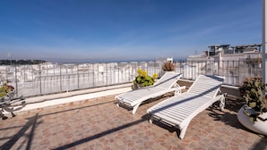 A rooftop terrace with two lounge chairs, a potted plant, and a view of the cityscape.