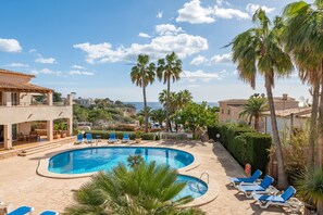 A pool area with lounge chairs, palm trees, and a view of the sea.