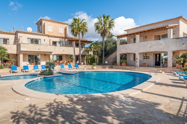 A swimming pool with lounge chairs, a building with balconies, and palm trees.