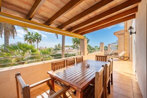 Una mesa y sillas de madera en un balcón con vista a palmeras y un edificio al fondo.