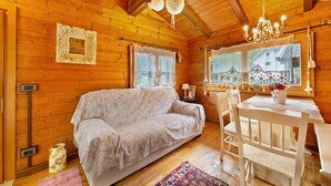 L’intérieur d’un chalet en bois, avec un canapé, une table à manger et des chaises, un lustre et une fenêtre donnant sur un paysage.