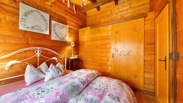 A wooden cabin bedroom with a bed, a nightstand, a lamp, and a wardrobe.