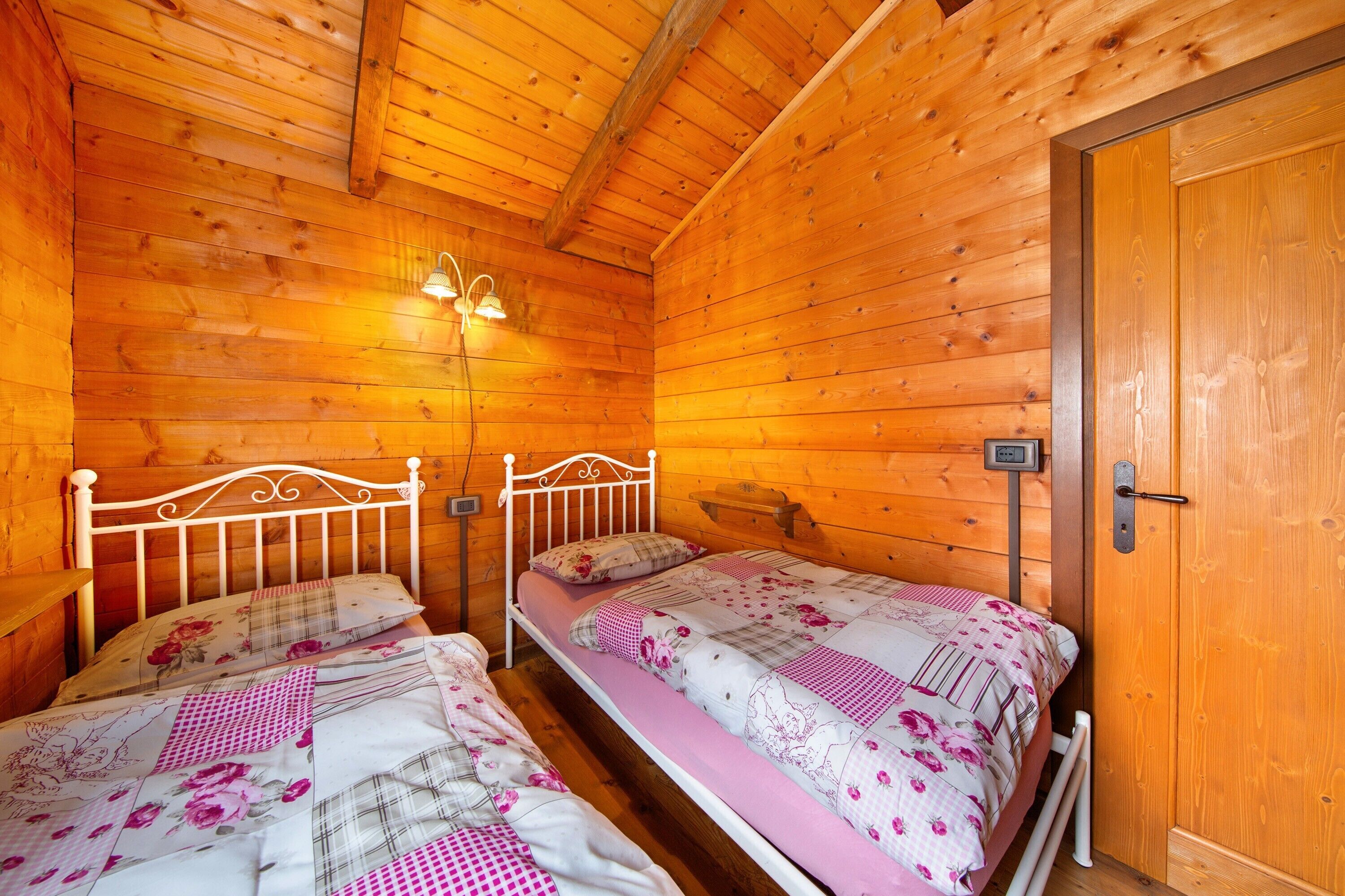 Ein Schlafzimmer in einer Holzhütte mit zwei Betten, einer Holzbalkendecke und einer Tür.
