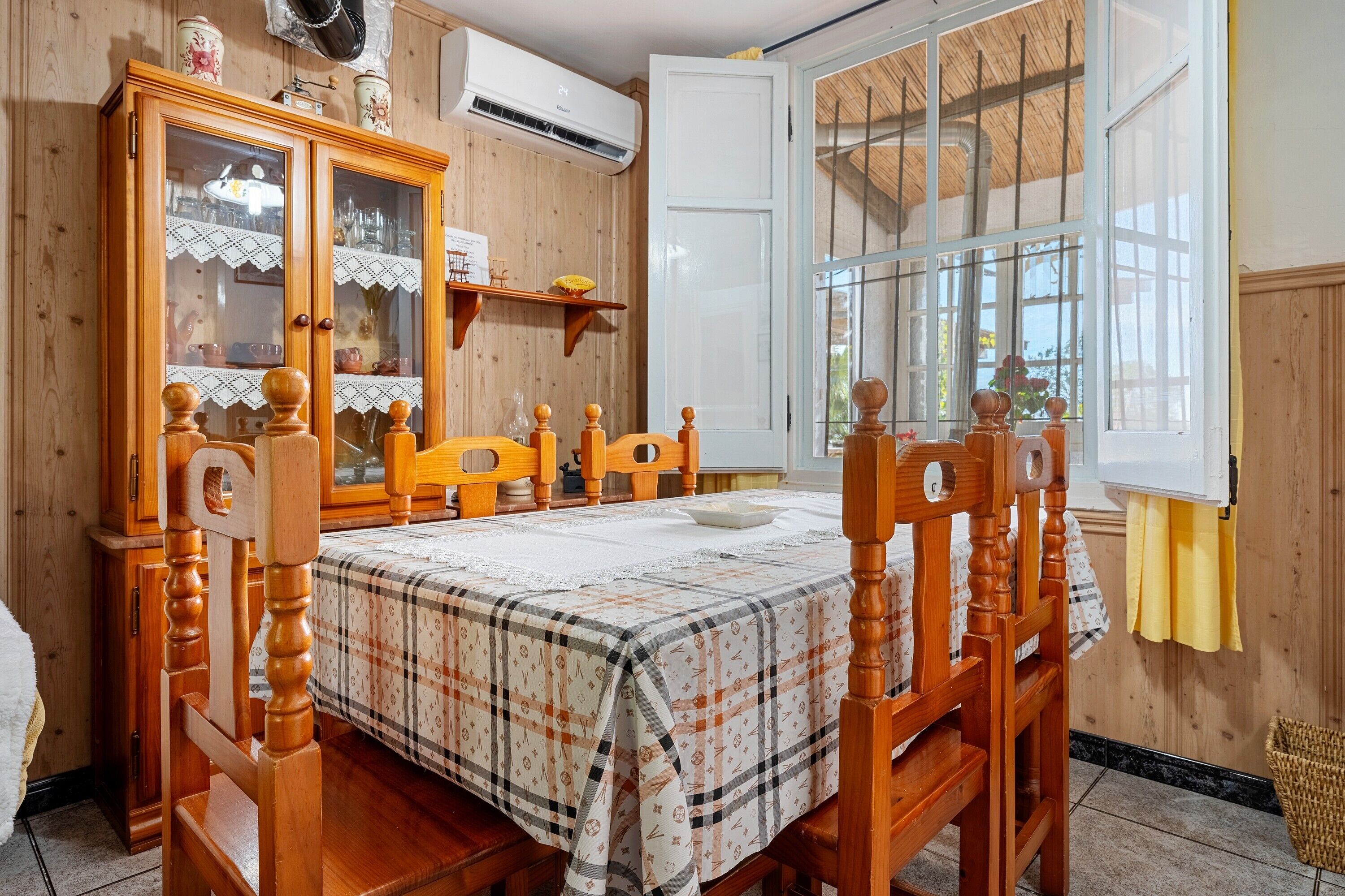 A dining room with a wooden table, chairs, a cabinet with glass doors, and a window with a view.