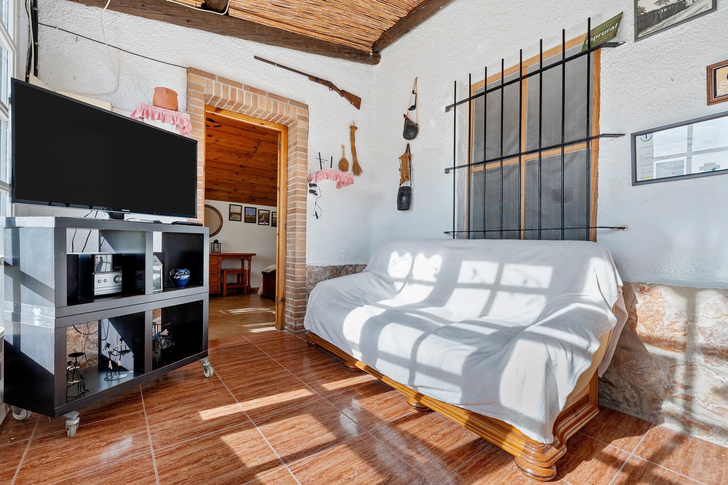 A room with a bed, a TV on a stand, a brick wall, and a window with bars.