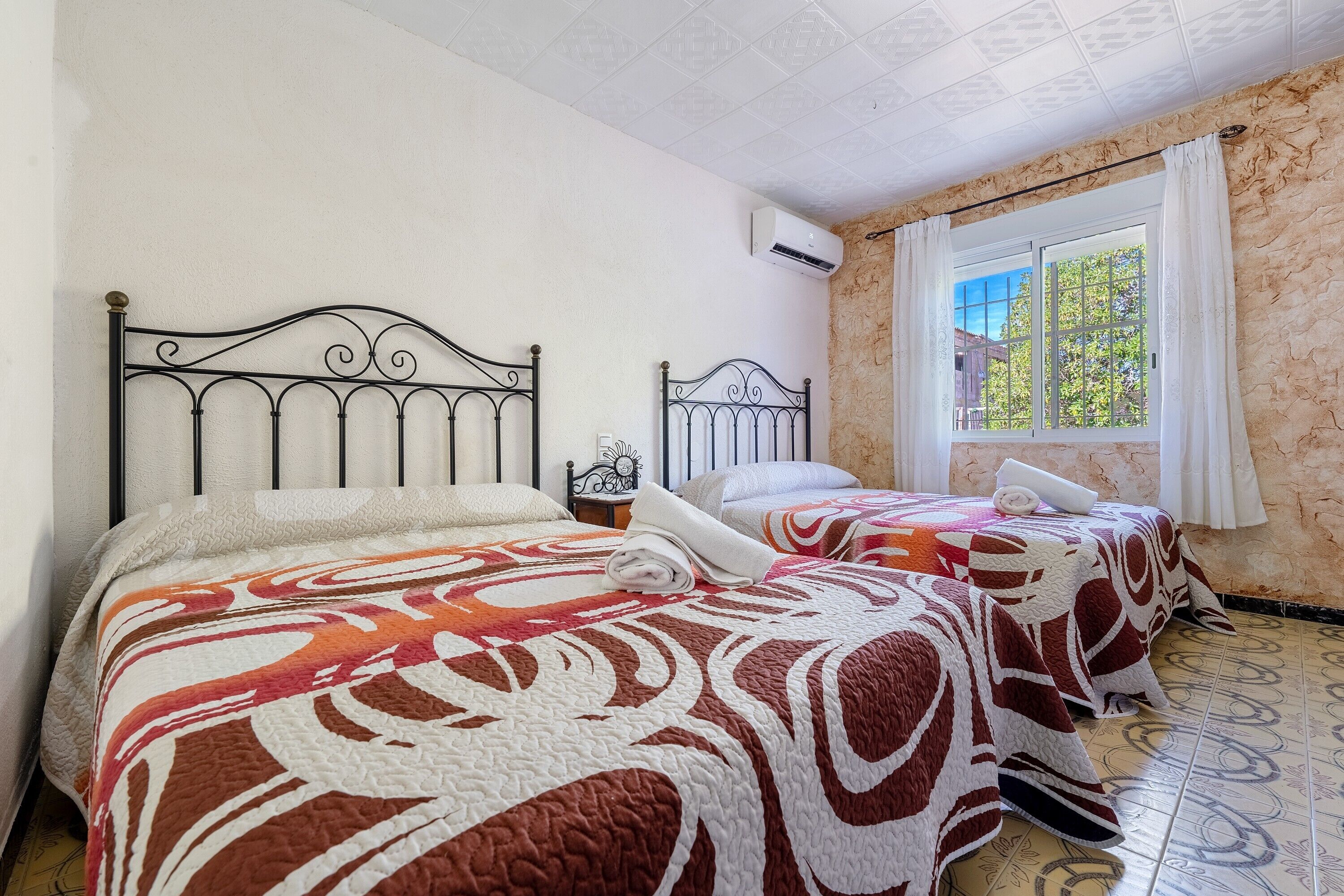 Dos camas con colchas estampadas, una ventana con cortinas y un equipo de aire acondicionado.
