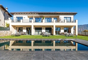 Une maison moderne à deux étages, dotée d’une piscine, d’un espace salon extérieur et offrant une vue sur les montagnes.