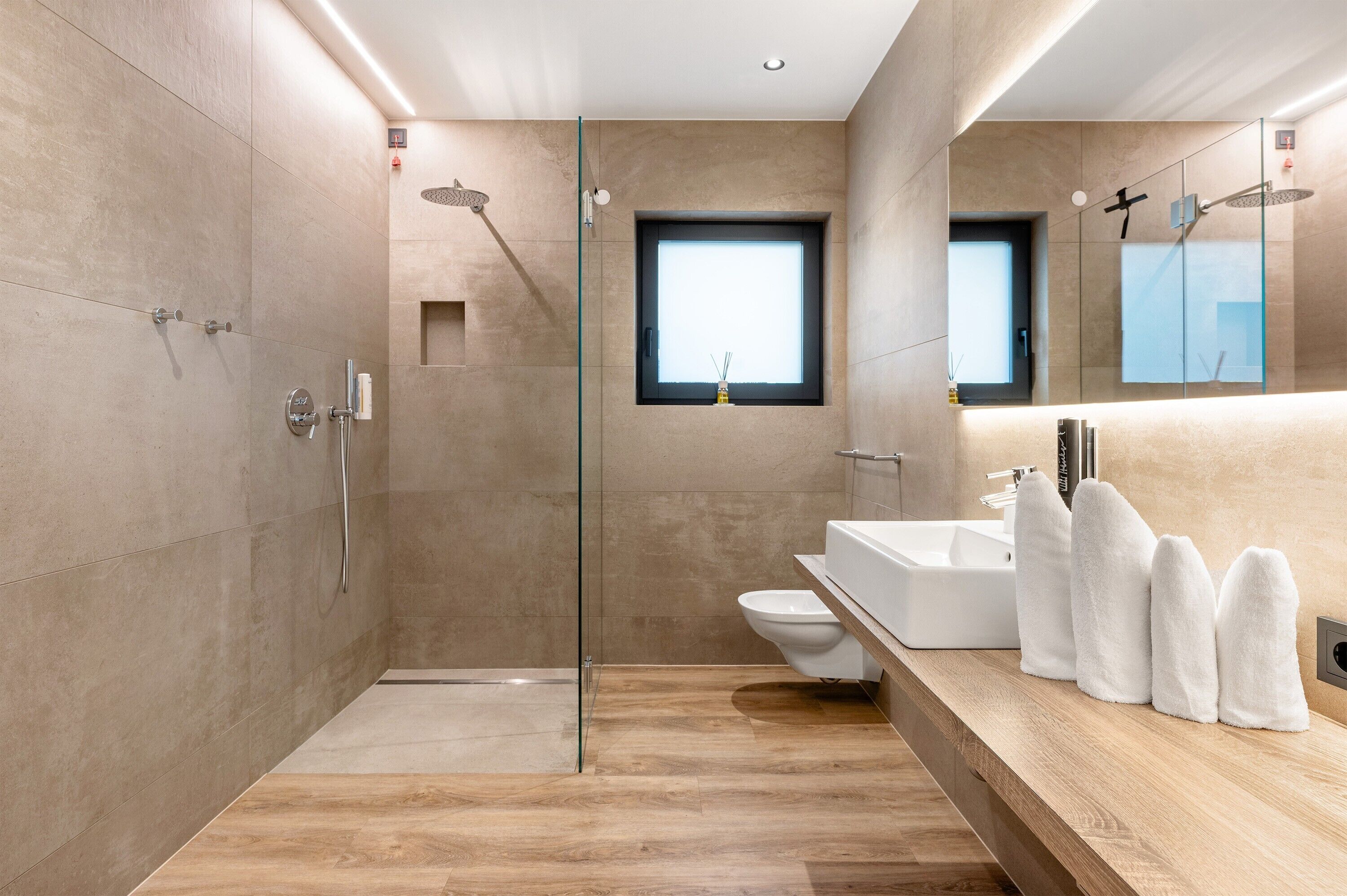 Ein modernes Badezimmer mit einer Duschkabine aus Glas, einem gro ßen Spiegel und einem Holzwaschtisch mit weißen Handtüchern.