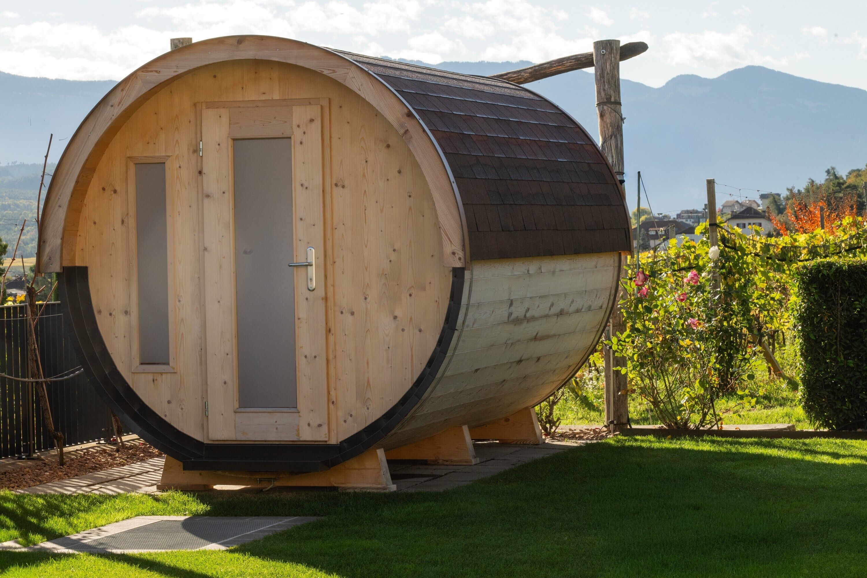 A cylindrical wooden structure with a door, situated in a grassy area with a mountain backdrop.