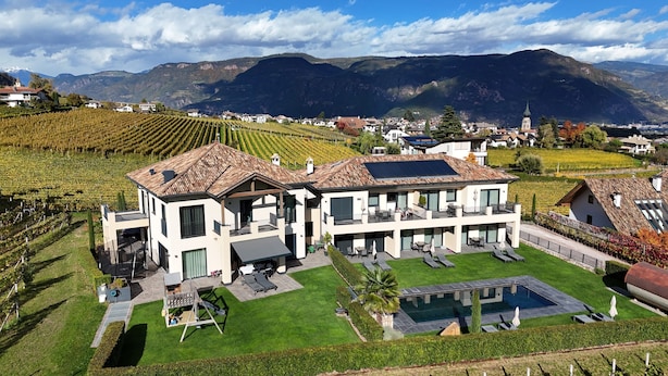 Una moderna casa a due piani con un ampio giardino, piscina e campi di vigneti sullo sfondo.