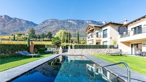Una piscina con vista libera sulle montagne sullo sfondo, un muro in pietra e un prato curato.