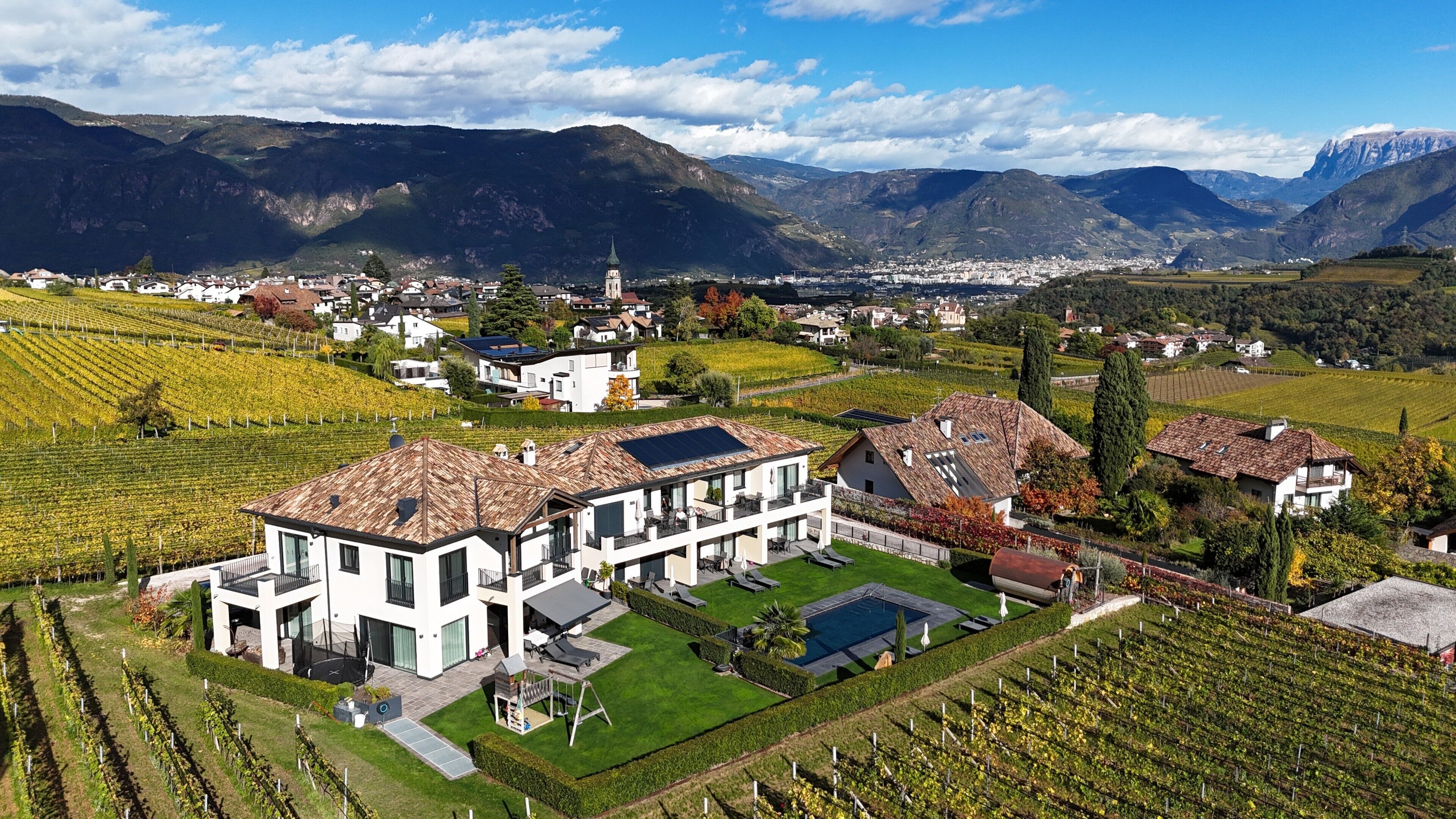 A modern two-story building with a large terrace, surrounded by vineyard fields and mountains in the background.