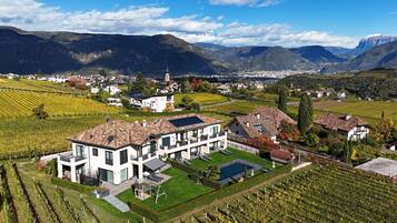 A modern two-story building with a large terrace, surrounded by vineyard fields and mountains in the background.