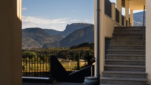 Eine Treppe führt zu einem Balkon mit Blick auf eine gebirgige Landschaft unter blauem Himmel.