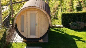 Ein zylindrisches Holgebäude mit einer Tür, umgeben von einem Garten und Weinbergen.