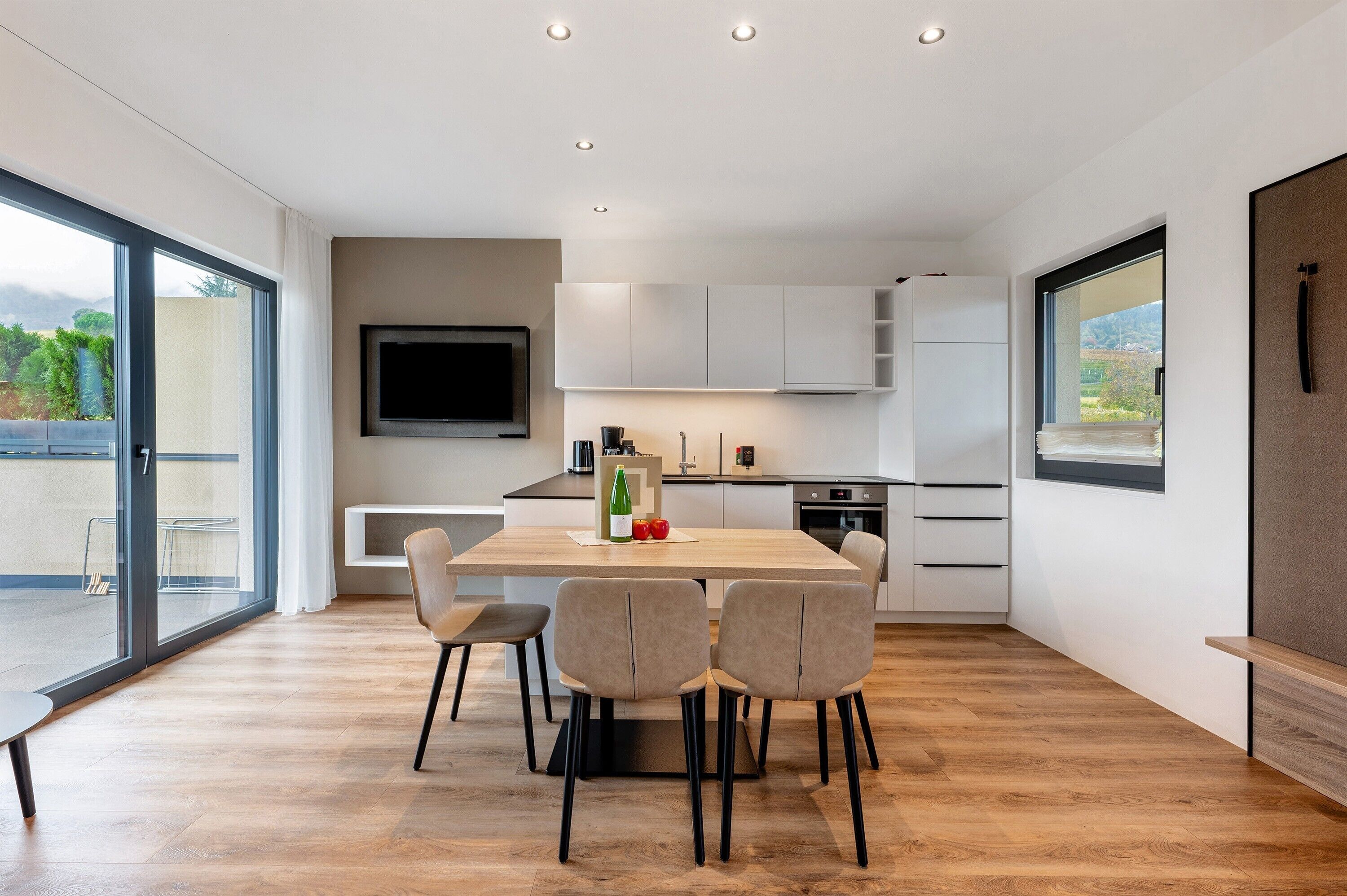 Een moderne keuken met een eethoek, grote ramen en een flatscreen televisie.