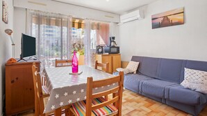 Ein Wohnzimmer mit einer Couch, einem Esstisch mit Stühlen, einem Fernseher und einem Gemälde an der Wand.